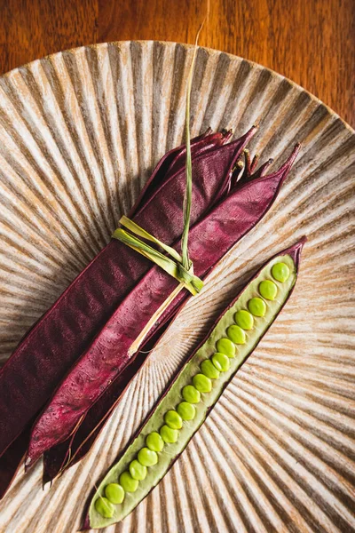 Açık tohumlu bir fasulye kabuğunun yanında tabakta duran bir demet mor Guaje fasulyesi. Oaxaca, Meksika.