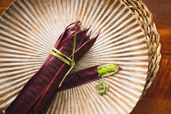 Açık tohumlu bir fasulye kabuğunun yanında tabakta duran bir demet mor Guaje fasulyesi. Oaxaca, Meksika.