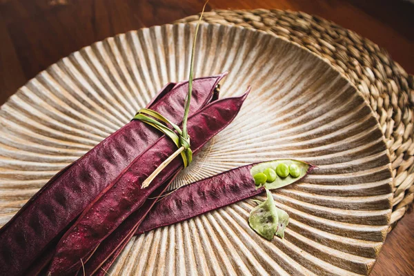 Açık tohumlu bir fasulye kabuğunun yanında tabakta duran bir demet mor Guaje fasulyesi. Oaxaca, Meksika.