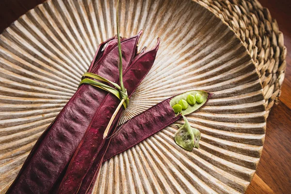 Açık tohumlu bir fasulye kabuğunun yanında tabakta duran bir demet mor Guaje fasulyesi. Oaxaca, Meksika.