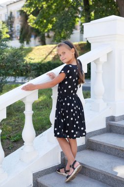 Bir yaz günü açık hava elbisesi içindeki sevimli, gülümseyen küçük bir kızın portresi. Kız gülümsüyor ve kameraya bakıyor.