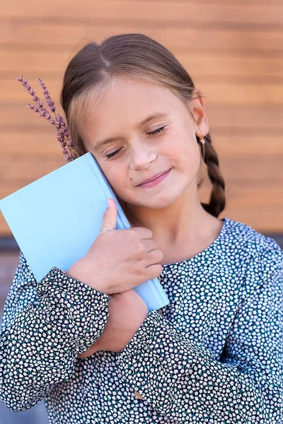 Porträt eines kleinen Mädchens mit einem Buch und getrockneten Blumen in ihren Händen. Sie umarmte das Buch und schloss die Augen. Träume. Fantasien. — Stockfoto