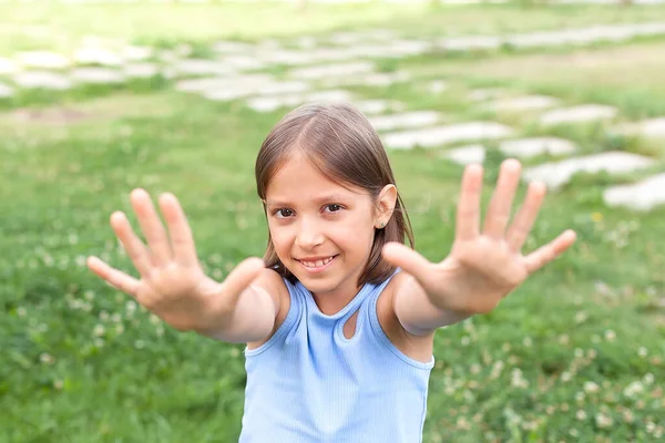 Uma menina alegre de 8-10 anos joga em um prado verde em um dia quente de verão, caminha ao ar livre, alegria e felicidade — Fotografia de Stock