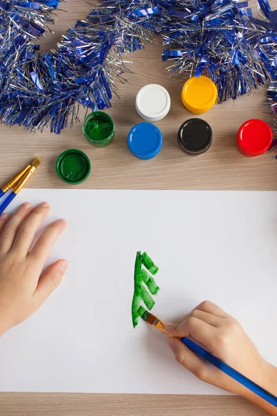 Een jongen schildert een kerstboom en sneeuw op een stuk papier. Kinderen Nieuwjaar tekening. Gouache en borstels. Ontwikkeling van het kind — Stockfoto