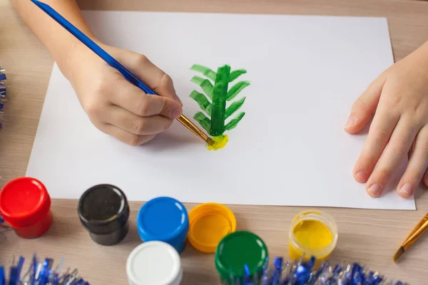 Un niño pinta un árbol de Navidad y nieve en un pedazo de papel. Dibujo de Año Nuevo para niños. Gouache y cepillos. Desarrollo infantil —  Fotos de Stock