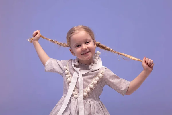 Leuk klein meisje in een ongewone jurk. Portret van een charmant meisje met vlechtjes in de studio. Een gelukkig meisje met een hoed lacht en kijkt naar de camera. Selectief scherpstellen en kleuren. — Stockfoto