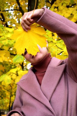 Sonbahar parkında sarı yapraklı bir arka planda ceketli bir kız.