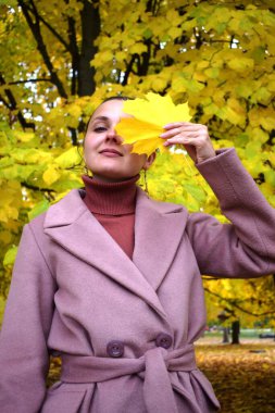 Sonbahar parkında sarı yapraklı bir arka planda ceketli bir kız.