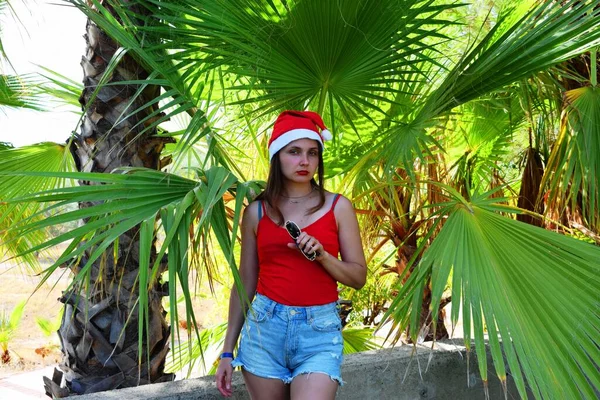 Girl Santa Claus Hat Red Shirt Background Green Palms Concept — Stock Photo, Image