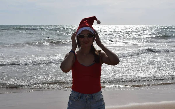 夜の海を背景にサンタクロースの帽子と赤いTシャツの女の子 暖かい国での新年とクリスマスの休日の概念 — ストック写真