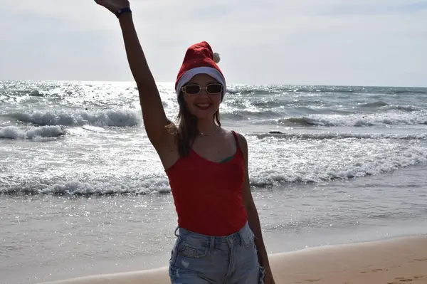 夜の海を背景にサンタクロースの帽子と赤いTシャツの女の子 暖かい国での新年とクリスマスの休日の概念 — ストック写真