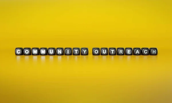 Words Community outreach spelled out in white text on dark wooden blocks against plain yellow background