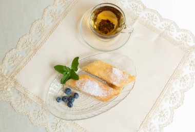 There is apple pie and tea on the table. The plate is decorated with blueberries and mint