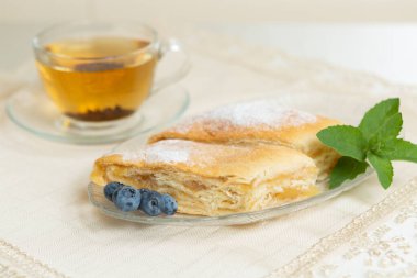 There are two slices of apple pie, blueberries and mint leaves on the plate, a cup of tea next to it