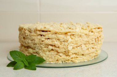 Homemade Napoleon Cake stands on the table in the kitchen. It is decorated with a sprig of mint