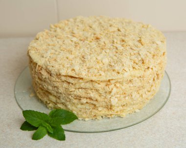 Homemade Napoleon Cake stands on the table in the kitchen. It is decorated with a sprig of mint
