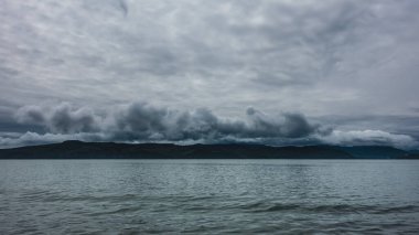 Pasifik kıyısında bir dağ sırası. Kara kümülüs bulutları gökyüzünde dönüyor. Okyanus yüzeyindeki dalgalar. Kamçatka.