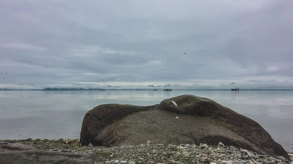 小石のビーチには巨大なぬれた岩とその上に羽があります 船は滑らかで光沢のある水を航行します 曇った空 ペトロパブロフスク カムチャツキー 太平洋 — ストック写真
