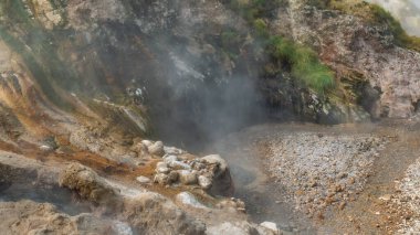 Gayzerler Vadisi sıcak pınarlardan gelen buharla kaplanmıştır. Dağın yamaçları sülfür tortularıyla kaplı. Kayalık bir yatak boyunca akarsular akar. Yakın plan. Kamçatka.