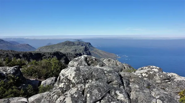 开普敦桌山山顶的风景 前景中有灰色斑点的巨石阵 远处可见芬伯斯灌木丛 蔚蓝的天空和蓝色的大西洋 — 图库照片