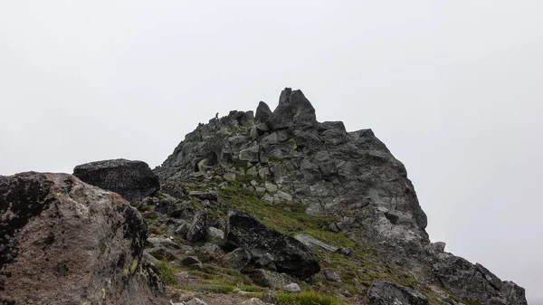 在雾蒙蒙的天空中 悬崖顶上有着奇异的轮廓 岩石上的裂缝和稀疏的植被 在山顶上可以看到一个男人的小轮廓 堪察加半岛骆驼山 — 图库照片