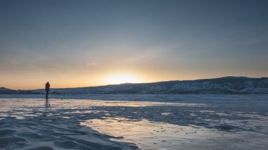 Batan güneş dağ sırasının üzerinden gökyüzünü turuncuya çevirir. Donmuş bir gölde yalnız bir adam var. Buzda parla. Baykal.