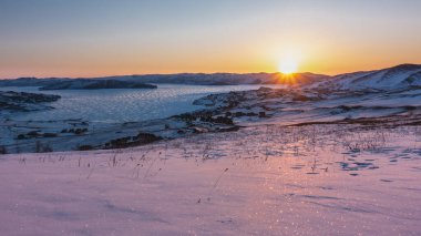 Yükselen güneşin ışınları dağ sırasını ve donmuş gölü aydınlatır. Gökyüzü turuncuyla işaretlenmiş. Buzda parla. Kıyıdaki kar parıldıyor. Sabah altın saati. Baykal.
