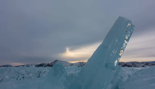 在结冰的湖面上 有几块绿松石岩石 一个巨大的浮冰在黄昏多云的天空背景下升起 太阳的光芒洒在边缘上 贝加尔湖 — 图库照片