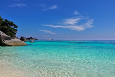 Temiz, şeffaf Andaman Denizi. Kumsal. Resimli kayalar suyun üzerinde yükseliyor. Güzel bulutları olan gök mavisi. Ufukta bir sürat teknesi beliriyor. Tayland 'da yaz günü. Similan Adaları.