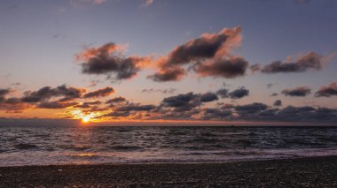 Deniz üzerinde endişe verici bir gün batımı. Güneş battı, alacakaranlık. Mor bulutlar kırmızıyla işaretlenmiş. Denizde, köpüklü dalgalar. Suda ve kumsaldaki çakıl taşlarında güneşli patika. Karadeniz.