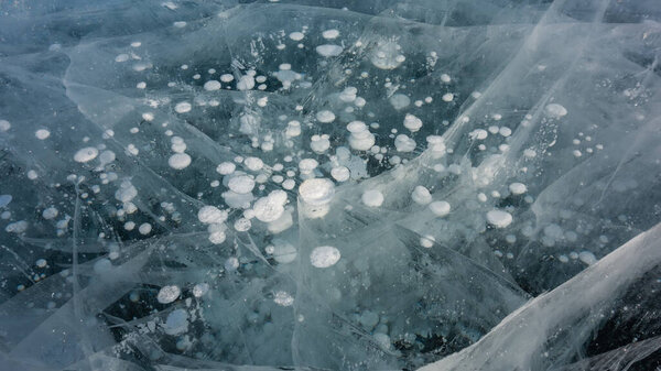 The surface of the clear turquoise ice. Close-up. Full screen. Bizarre deep intersecting cracks. Bubbles of frozen methane gas. Lake Baikal