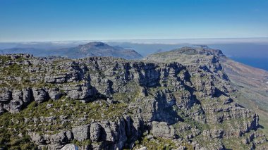 Cape Town 'daki Masa Dağı' nın tepesinde gri taşlar arasında çalılıklar görülebilir. Yamaçlarda çatlaklar var. Mavi gökyüzü. Güney Afrika