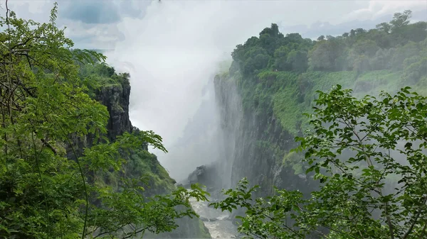 ビクトリア滝からの濃い霧が渓谷の上にスプレーしています 峡谷の底には嵐の川が流れている 周りに緑の植生があります ジンバブエ — ストック写真