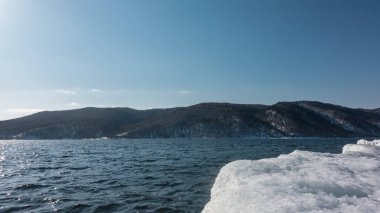 Karla kaplı kıyılar arasında buzsuz mavi bir nehir akıyor. Dalgalar ve güneş suda parlıyor. Gök kubbeye karşı bir dağ sırası. Angara. 