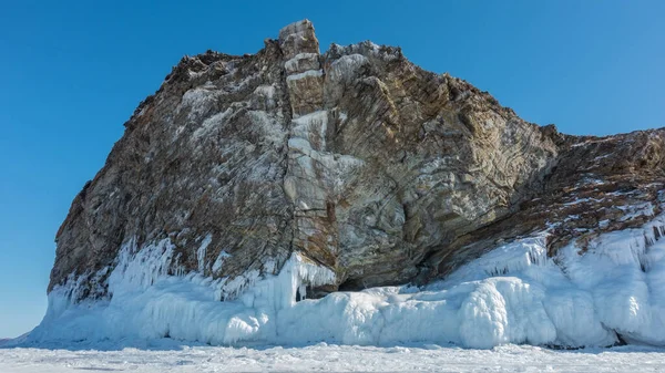 澄んだ青い空に対して 植生のない絵の花崗岩の岩 石の斜面に亀裂 ベースには太いつららの層 凍結した湖の周りの氷 バイカル — ストック写真