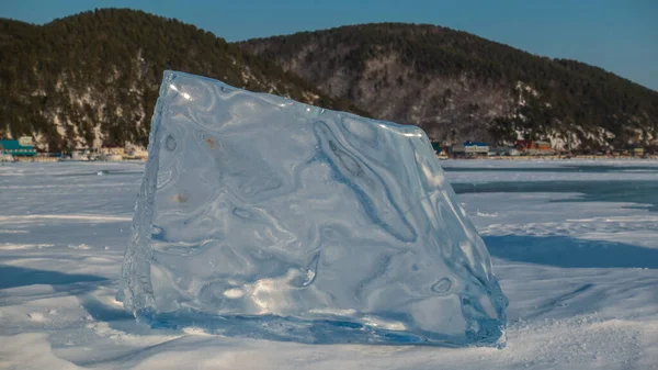 一个巨大的闪亮的浮冰垂直地站在一个结冰覆盖的湖上 阳光照射在边缘上 在远处 蓝色的天空映衬着一片茂密的山脉 贝加尔湖 — 图库照片