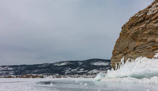 植生のない花崗岩の岩は 凍った湖の上に隆起する ベースには太いつららの層があります 氷の上の破片 青い空に対する山の範囲 バイカル — ストック写真