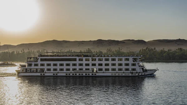 Beyaz bir yolcu gemisi Nil Nehri 'nde yelken açıyor. Akşam güneşi kıyı kum tepelerinin üzerinde parlıyor. Suda yansıma. Mısır