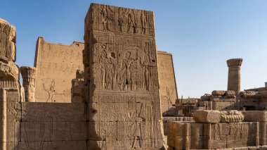 Edfu 'daki antik Mısır tapınağı Horus' un kalıntıları. Harap olmuş duvarlara insan figürleri ve hiyeroglifler kazınmış. Mavi gökyüzü. Güneşli bir gün.