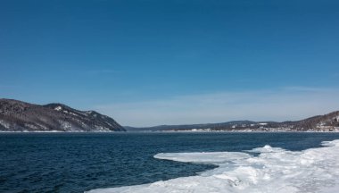 Mavi buzsuz nehir Angara buzlu kıyılar arasında akar. Sudaki dalgalanmalar. Gök mavisi gökyüzüne karşı bir dağ sırası. Uzayı kopyala Sibirya