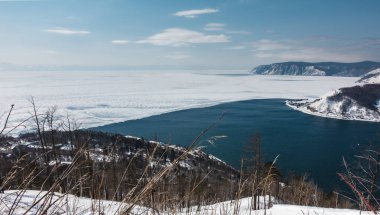 Buzsuz Angara Nehri donmuş Baykal Gölü 'nden akar. Beyaz buz ve mavi su arasındaki zıtlık. Gök mavisi gökyüzüne karşı dağlar. Kıyıda kar ve kuru çimenler. Sibirya