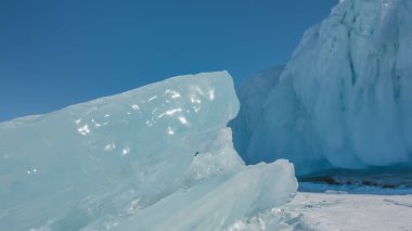 A thick shiny turquoise ice floe against the blue sky. The glare of the sun on the edges. Close-up. In detail. Background - blue sky, icy rock. Baikal