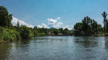 The blue River flows calmly. Ripples on the water. Lush green vegetation on the banks. Cumulus clouds in the azure sky. Kamchatka