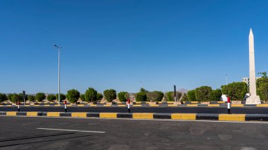 Otoyolun yeni asfaltı ve bölünen şeride beyaz, sarı ve siyah işaretler uygulanır. Yol kenarında yeşil çalılar yetişiyor. Açık mavi gökyüzü. Mısır