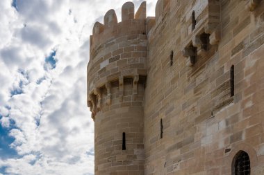Kadim Qaitbay Kalesi 'nin duvarının bir parçası mavi gökyüzü ve bulutlardan oluşan bir arka plana karşı. Görünür taş ustası, dar kemerli pencereler. İskenderiye. Mısır.