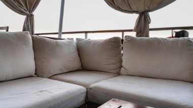 Bir turist gemisinin güvertesinde dinlenme alanı. Yastıklı bej renkli kanepe. Perdeler parmaklıkların üzerinde bağlı. Mısır