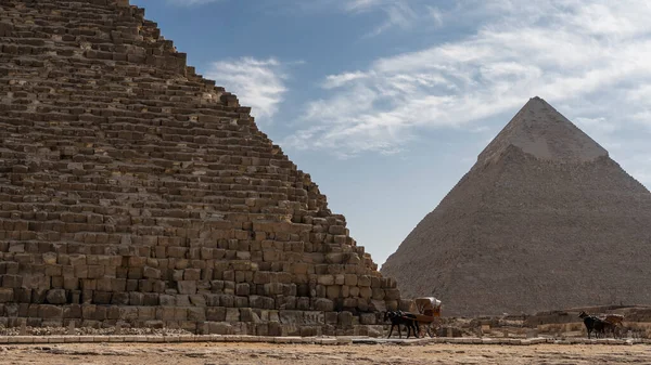 Giza CheopsとChephrenの2つの大きなピラミッドは青い空に対して 古代の石積みの壁が見える 足では馬のカートに使用されます エジプト — ストック写真