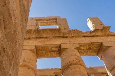 Luxor 'daki antik Karnak tapınağının bir parçası. Mavi gökyüzü arka planına karşı bir duvar ve kolonlar. Oymalar, hiyeroglifler görünür. Mısır