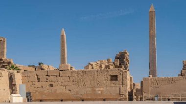 Luxor 'daki Karnak Tapınağı' nın harap olmuş duvarlarında hiyeroglifler ve oymalar görülebilir. Açık mavi gökyüzüne karşı iki dikilitaş yükselir. Mısır