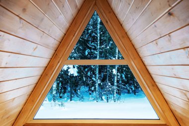 Kışın ormana bakan ahşap üçgen pencere.